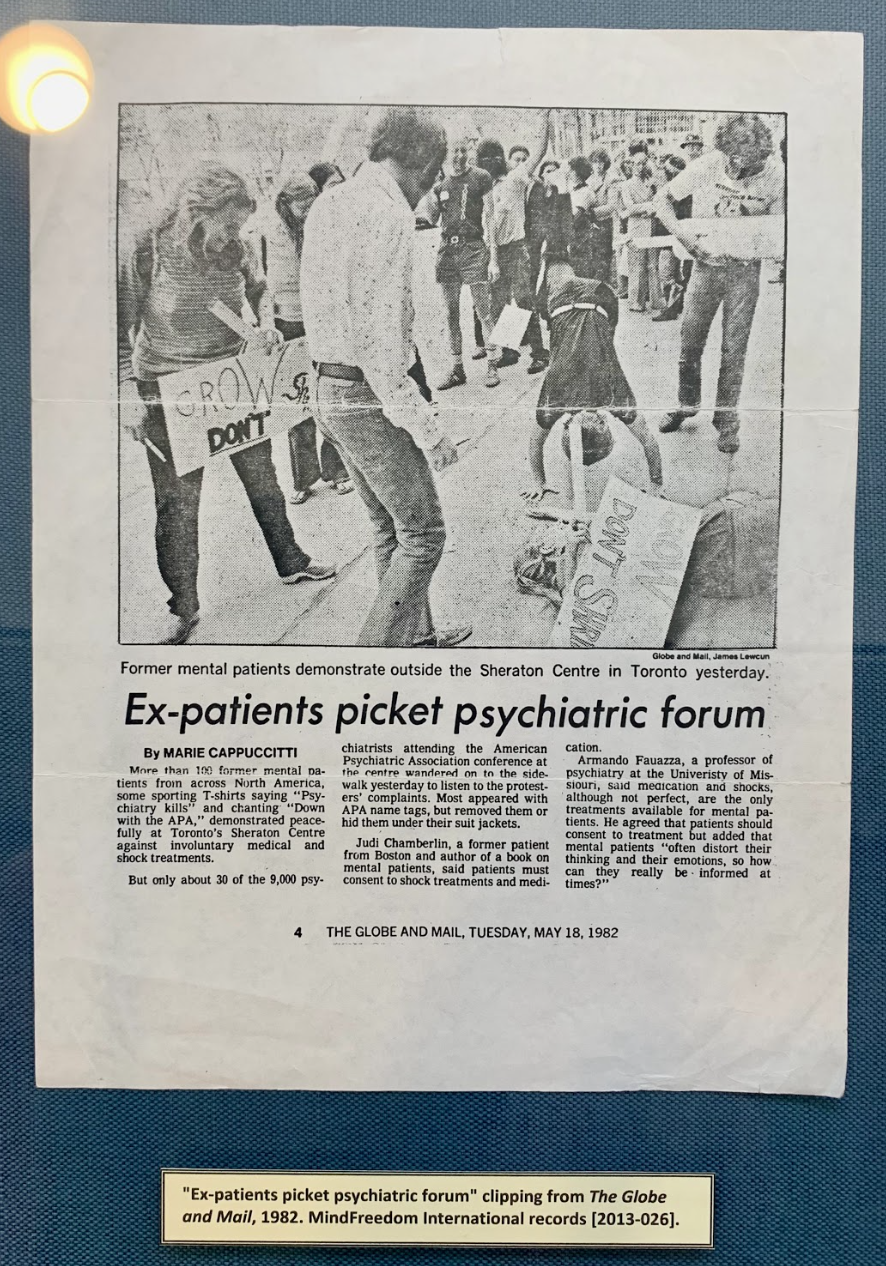 This image is a picture taken at the OHSU exhibit. It is an older, slightly stained newspaper published by the Globe and Mail. In the newspaper clipping, there is a featured photograph of individuals protesting against the APA. Men and women are gathered and smiling, holding signage. The newspaper's text below the picture describes how only 30 of the 9,000 psychiatrists came out from their conference at the APA to converse with protesters.